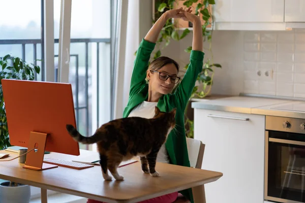 木のテーブルに座っている若い女性は 観葉植物と自宅のオフィスでコンピュータ上で作業した後に残ります 注目を集める猫に邪魔された実業家 女性は遠くの仕事から体を伸ばす ペット愛好家 — ストック写真
