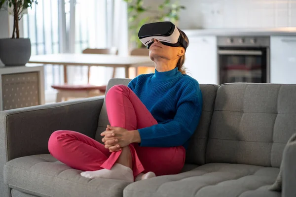 好奇的欧洲女人在辛辛苦苦工作了一天后 戴着虚拟现实眼镜放松了下来 女孩坐在餐厅旁边的沙发上 用创新的Vr和Ar技术目不转睛地观看视频 — 图库照片