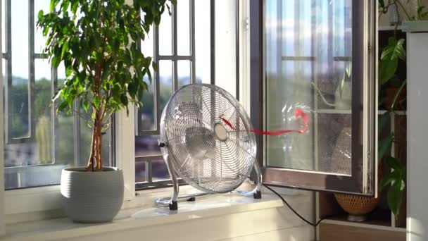 设计用于冷却空气和供风的带有红色扭带的工作电扇位于工厂旁边的窗台上 炎热夏季室内降温设备 — 图库视频影像