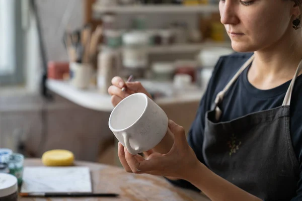 白いマグカップに未来の模様をスケッチする工房で 職人が新たな名作を生み出します 女性のマスターは 興味深いパターンを描くために鉛筆を使用して塗装粘土料理とキッチンを飾るしたい — ストック写真