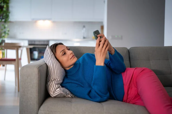 Klidná Žena Modrém Svetru Svitky Sociálních Médií Smartphone Těší Relaxaci — Stock fotografie