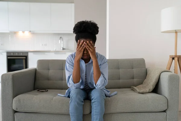ストレスに苦しんでいるアフリカ系アメリカ人女性を圧迫し 手で目を閉じてアパートのソファに座っています 心理的な問題を抱えている若い女の子は仕事を失った後に心理学者の助けが必要です — ストック写真