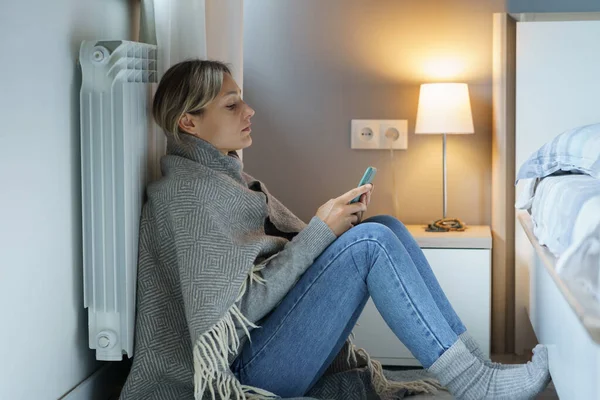 Tired young woman covered with warm blanket searches Internet looking for job to have opportunity to pay bills. Pensive female leaning back on battery wants to prevent bankruptcy trying to find job