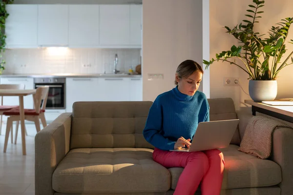 身穿蓝色毛衣的女自由职业者在笔记本电脑上为未来的商业项目工作 集中表达的女商人坐在舒适的沙发上 在网上创作创业草稿 — 图库照片