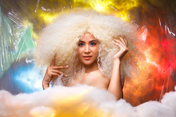 Half Body Portrait of 20s Asian Caucasian beautiful Woman blonde afro hair high fashion make up. Cute Girl smile look at camera over pastel red blue yellow colorful sky cloud in studio