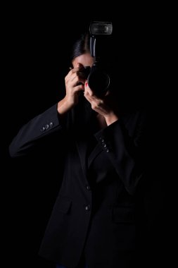 Asyalı Kadın Fotoğrafçı, fotoğraf çekmek için kamerayı dış ışık noktasından tut, resmi kıyafet giy. Stüdyo aydınlatma siyah arkaplan izole fotokopi alanı, muhabir fotoğraf ünlüsü aldı