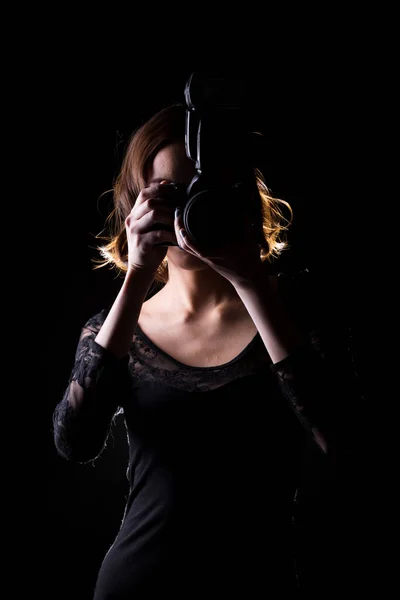 亚洲女摄影师手持相机与外部闪点拍摄的主题 身穿紧身衣 摄影棚点亮黑色背景隔离低调曝光记者拍照名人 — 图库照片