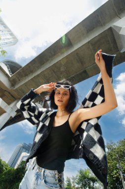 20 'li yaşlardaki Asyalı kahverengi saçlı kadının portresi mavi gökyüzü bulutu altında yüksek moda ceket giyiyor. Güzel kadın duygularını ifade ediyor. Tren istasyonunda mutlu bir gülümseme.