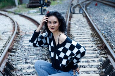 20 'li yaşlardaki Asyalı kahverengi saçlı kadının portresi mavi gökyüzü bulutu altında yüksek moda ceket giyiyor. Güzel kadın duygularını ifade ediyor. Tren istasyonunda mutlu bir gülümseme.