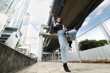 20 'li yaşlardaki Asyalı kahverengi saçlı kadının portresi mavi gökyüzü bulutu altında yüksek moda ceket giyiyor. Güzel kadın duygularını ifade ediyor. Tren istasyonunda mutlu bir gülümseme.