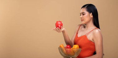 Uzun siyah düz saçlı, uzun dişli gülümseyen, sağlıklı taze yiyecek meyveleri ve beyaz diş tebessümlü sepetli mutlu bir Asyalı kadın. Bej sarısı arkaplan kopyalama alanı