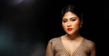 Asyalı 20 'li yaşlarda şişman bir kadın siyah kürk ceket, kırmızı dudaklar ve siyah arka planda çiller giyiyor. Yarı vücut, siyah saç ekspresi. Stüdyo ışıklarında yüzünde güçlü bir gülümseme hissediyor.