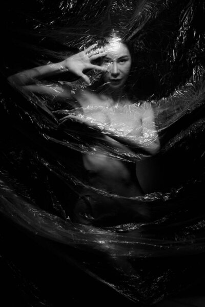 Nudity Slim woman emotionally posing, wrapped close to the fresh and fitting her sensual full body plastic film. Style artistic, abstract design, creativity. Monochrome Black and white