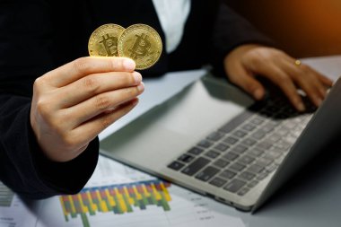 İş kadını, Bitcoin kripto para biriminin gerçek madeni parasını elinde tutarak özgürlüğünü veya merkezsizleştirilmiş finansmanı sunar, siyah arkaplan üzerinde bilgisayar dizüstü bilgisayar hesap makinesi grafiğiyle kopyalama alanı oluşturur.