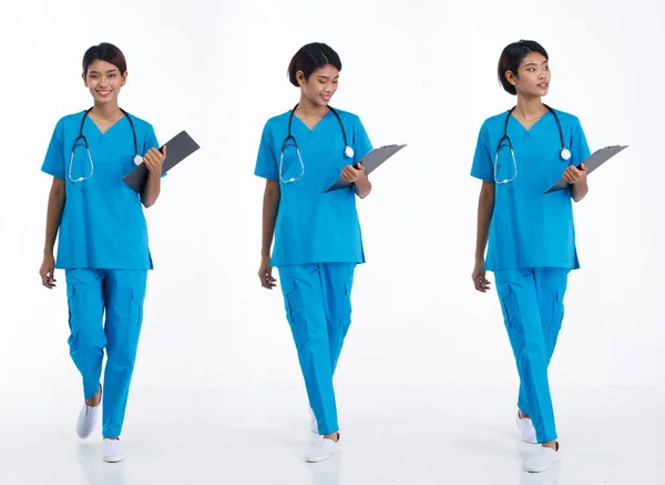 全长20多岁的年轻亚洲女护士佩戴听诊器 蓝色制服 向右左前行走 医院女病人携带病历资料快乐地笑过白底隔离 — 图库照片
