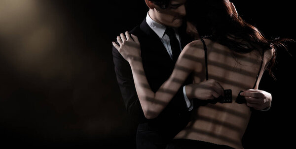 Young Couple embraces with love, business man try to untie lingeries bra of girlfriend. Sexy female hug working suit male gently over dark smoke background isolated, low exposure copy space