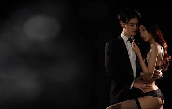Young Couple embraces with love, business man try to untie lingeries bra of girlfriend. Sexy female hug working suit male gently over dark smoke background isolated, low exposure copy space
