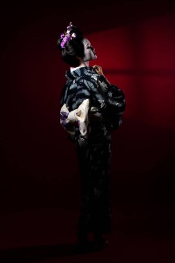 20 'li yaşlarda Asyalı bir kadın geleneksel mavi kimono giyer ve duvar camına geri döner. Japon Kimono kadın ekspres mutlu zen düşüşü kırmızı gölge arkaplan izole kopya alanı