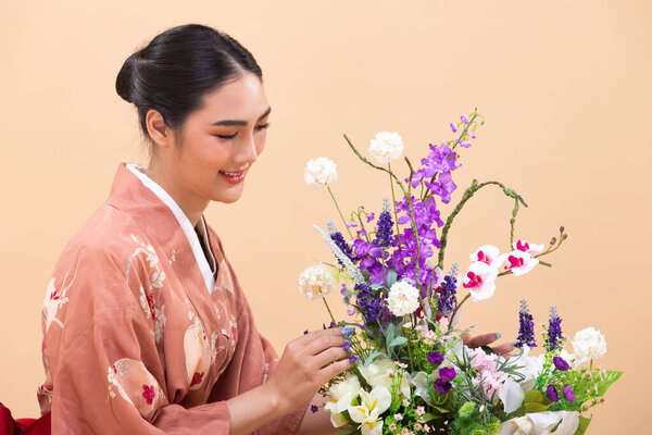 Young 20s Asian Japanese woman wear Pink traditional Kimono, does Ikebana flower arrangement. Japan Kimono female express felling happy smile over pastel yellow background isolated copy space