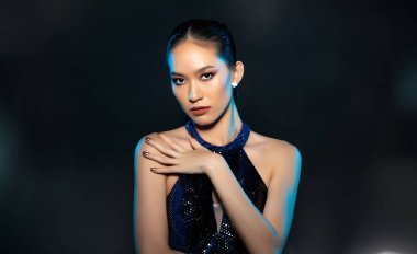 Half body of Asian beautiful woman wear blue evening sequin gown, fashion vintage poses. Young female stand express feeling happy smile strong over black background isolated copy space