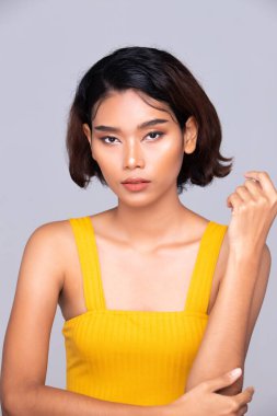 Beautiful Tanned skin woman wear yellow dress open shoulder with clean look make up and curl hair. Portrait young girl in attractive natural fashion face express feel smile, isolated gray background