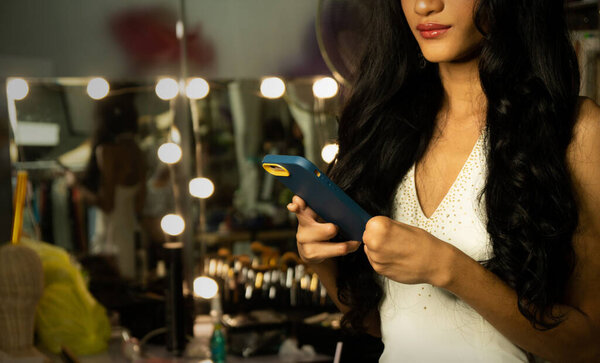 Half body disable person without fingers thumb hand of young adult woman using internet phone text chat at make up mirror desk. Female smile cheerful in white evening gown ball dress long hair