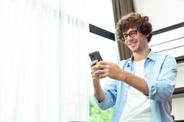 Young Caucasian Man work from home on laptop and connect online to office indoor for remote internet workplace. Young Adult male  communicate text chat on phone in living room, copy space