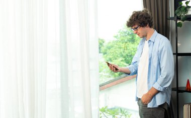 Young Caucasian Man work from home on laptop and connect online to office indoor for remote internet workplace. Young Adult male  communicate text chat on phone in living room, copy space