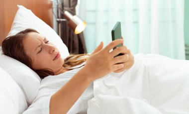 Caucasian woman sleep on bed pillow and phone wake up alarm. Female feel sleepy and shock when pick up smart phone and watch time to work in dawn morning. Young Adult express feeling shock, copy space