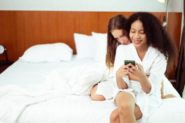 Caucasian and black women love together and hug hold as diversity person. Young Adult Romantic couple look at smart phone photo chat text as focus at blonde hair girl, copy space