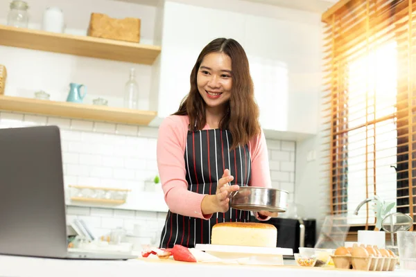 Asian young adult woman learn how to bakery cooking cake online course in kitchen. Female mother video to cyberspace class on laptop as blogger social media content and streaming learning, copy space