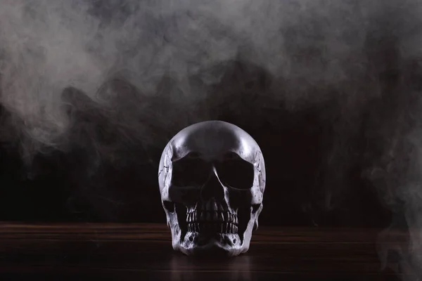 万圣节人类头骨在黑色背景的旧木制桌子上 在狂欢节之间 骷髅头的形状显示出可怕的恶牙恐惧和烟雾的恐怖 复制空间 — 图库照片