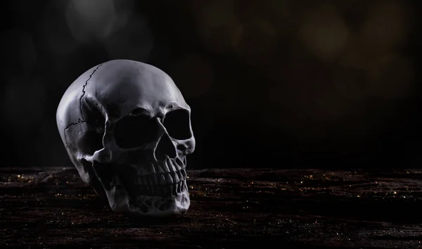 黒い背景の上に古い木製のテーブルの上にハロウィーンの人間の頭蓋骨 恐ろしい邪悪な歯の恐怖と霧の煙で怖いを示すハロウィーンの祭りで頭のための頭蓋骨の骨の骨の形 コピースペース — ストック写真