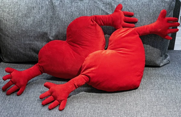 Två Röda Plysch Kuddar Form Hjärtan Med Händerna Grå Soffa — Stockfoto