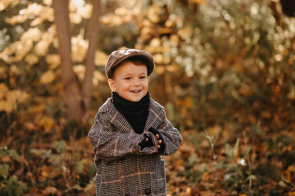 Un ragazzo bambino felice e candido in un cappotto autunnale cammina in un parco giallo autunnale. — Foto Stock