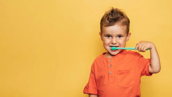 Menino bebê feliz escovando os dentes com uma escova de dentes em um fundo amarelo. Saúde, higiene oral. Um lugar para o seu texto. — Fotografia de Stock
