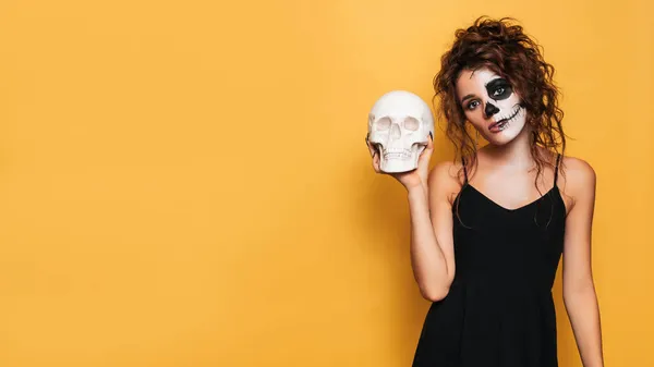 Estúdio tiro de uma menina em um traje de espíritos malignos em uma festa de fantasia de Halloween com um crânio em suas mãos. Um lugar para o seu texto para produtos, publicidade. A arte do Halloween — Fotografia de Stock