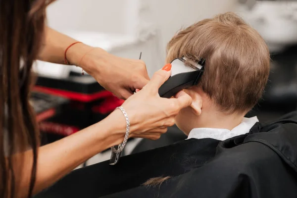 A filmar num salão de beleza. Um barbeiro corta o cabelo de um menino com uma máquina. — Fotografia de Stock