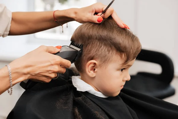 A filmar num salão de beleza. Um barbeiro corta o cabelo de um menino com uma máquina. — Fotografia de Stock