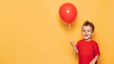 Parlak sarı arka planda izole edilmiş mutlu bir beyaz çocuk elinde kırmızı bir balon tutuyor. Mesajınız ya da ilanınız için bir yer.