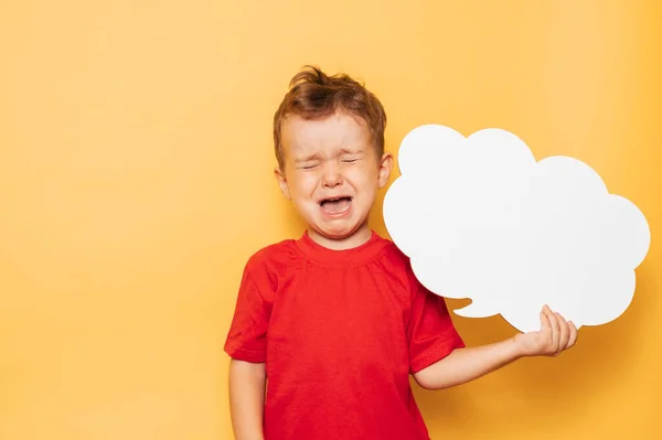 Studio portrait of a crying boy with a clean white board in the shape of a cloud on a bright yellow background, with a place for your text or advertising — Stock Photo, Image