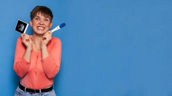 Una mujer embarazada alegre sostiene una imagen de ultrasonido del bebé y la prueba sobre un fondo amarillo. Sonograma. Copiando espacio. El concepto de embarazo y salud materna. —  Fotos de Stock