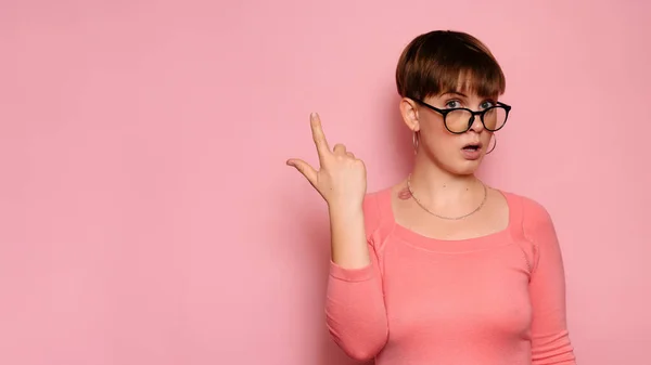 Portrait of a surprised attractive Caucasian girl isolated on a pink background, pointing up in amazement. Space for copying. Advertisement. — Zdjęcie stockowe