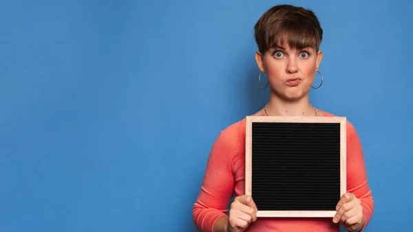 Studio shot of a young woman with a skeptical expression holding a blank letter board on a blue background. Copy space, space for your ad or text. — Zdjęcie stockowe