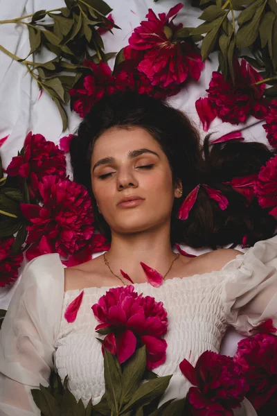 散在する花、牡丹に囲まれて横たわっている若い、平和で穏やかな女の子の肖像画。トップ表示 — ストック写真