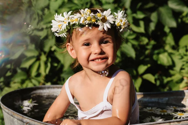 Un lindo bebé sonriente se está bañando en una bañera de pie en el jardín, en un día de verano soleado caliente —  Fotos de Stock