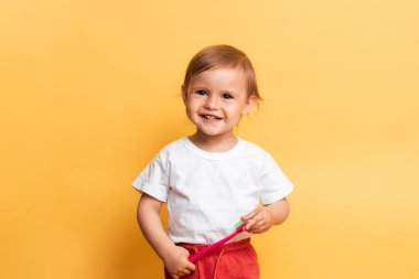 Diş hijyeni kavramı. Küçük sarışın kız dişlerini diş macunuyla fırçalıyor. Sarı arkaplan.