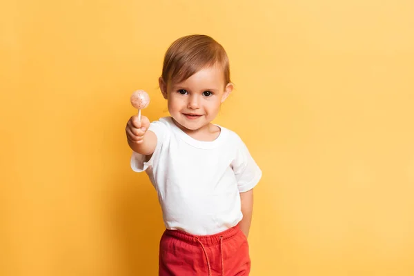 Uma menina está comendo um doce chupa-chupa em um pau. Fundo amarelo. O conceito de prevenção da cárie e diabetes em crianças. — Fotografia de Stock