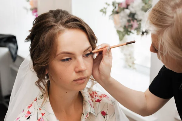 A filmar num salão de beleza. artista de maquiagem faz uma maquiagem de casamento para uma jovem menina bonita. — Fotografia de Stock