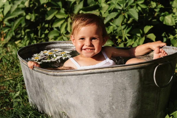 Una niña sonriente se está bañando en una bañera de pie en el jardín, en un día caluroso y soleado de verano —  Fotos de Stock